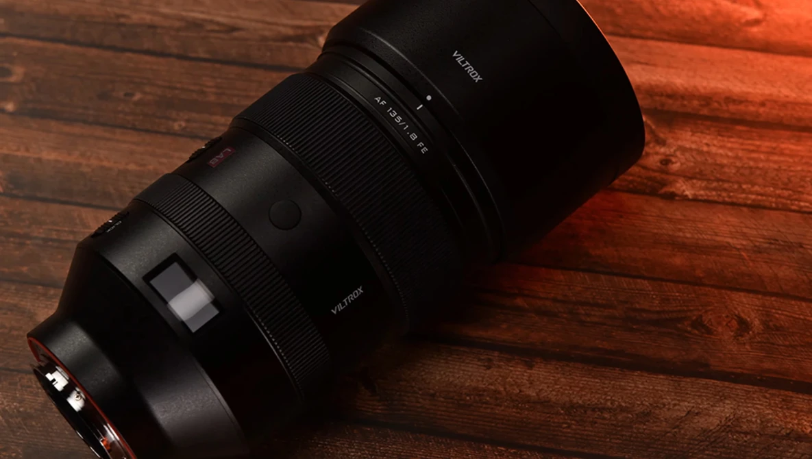 Black telephoto lens with focus ring and aperture markings displayed on warm wooden surface.