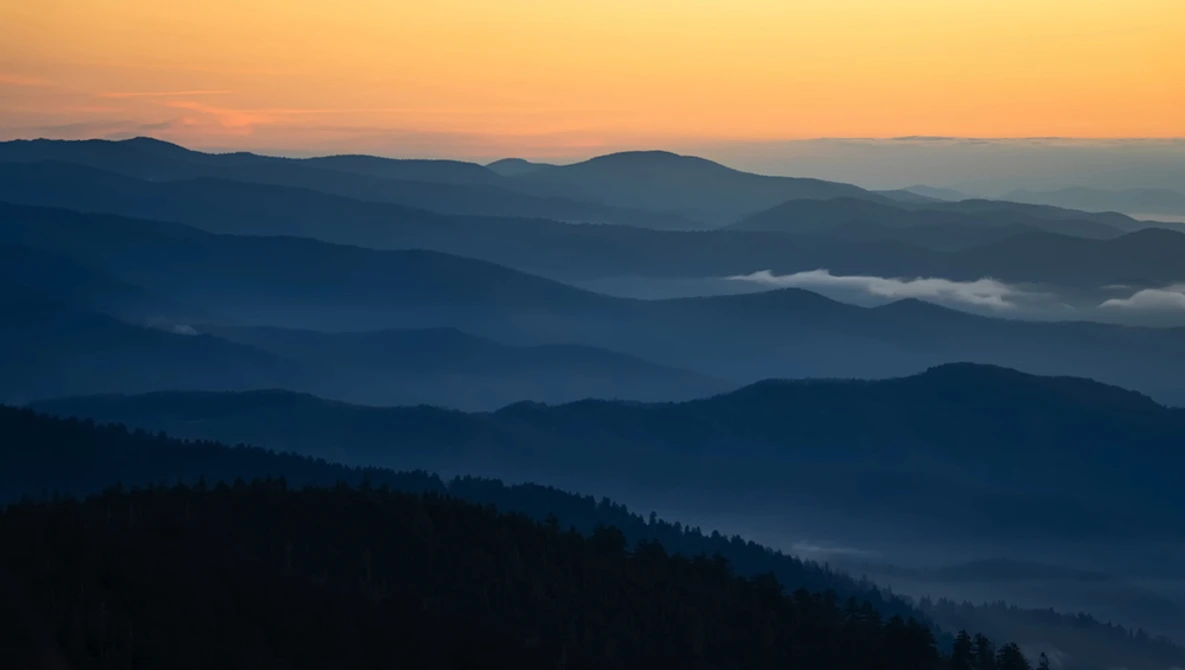 Layered mountain ridges receding into hazy distance under golden sunrise sky.