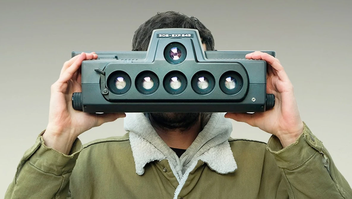 Photographer holding a panoramic film camera with six lenses across its front.