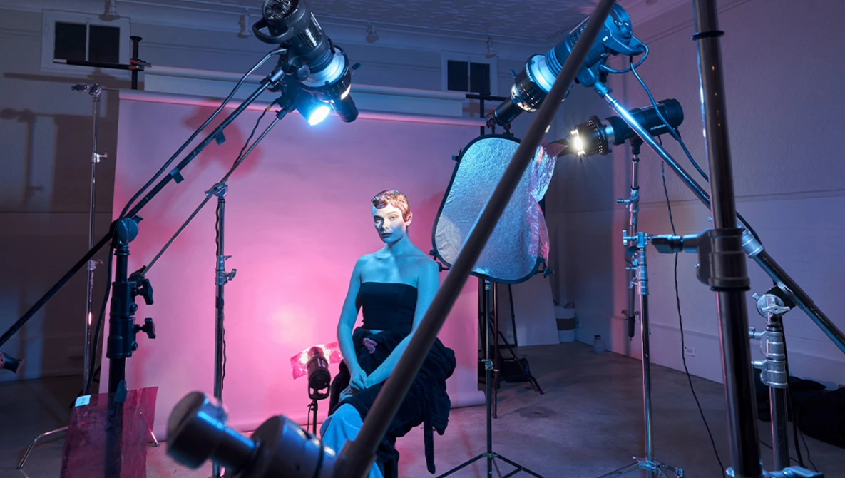 Studio portrait lit with multiple professional lights creating a pink and blue color cast on the subject.