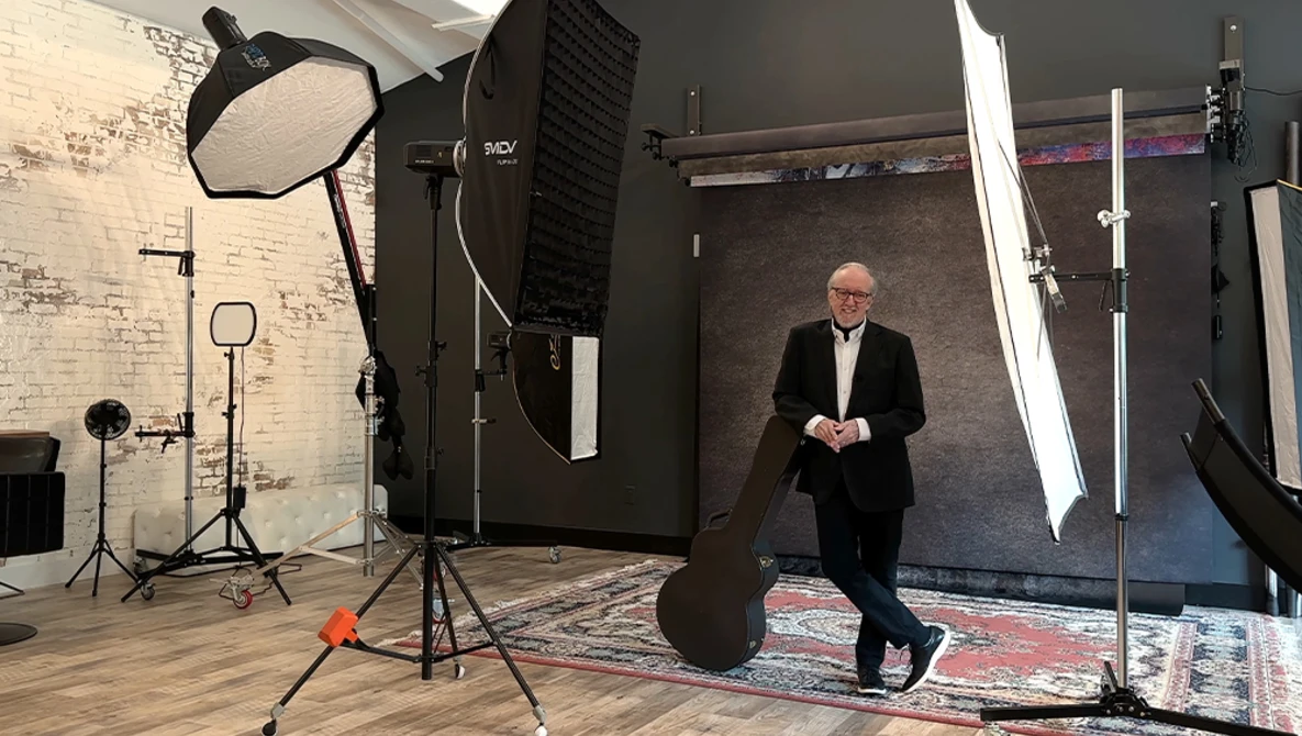 Man in business attire standing in a professional photography studio with softbox lighting and reflector equipment.