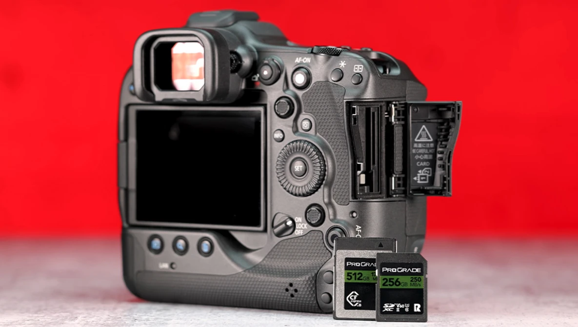 Professional mirrorless camera with open battery door and two memory cards displayed on red background.