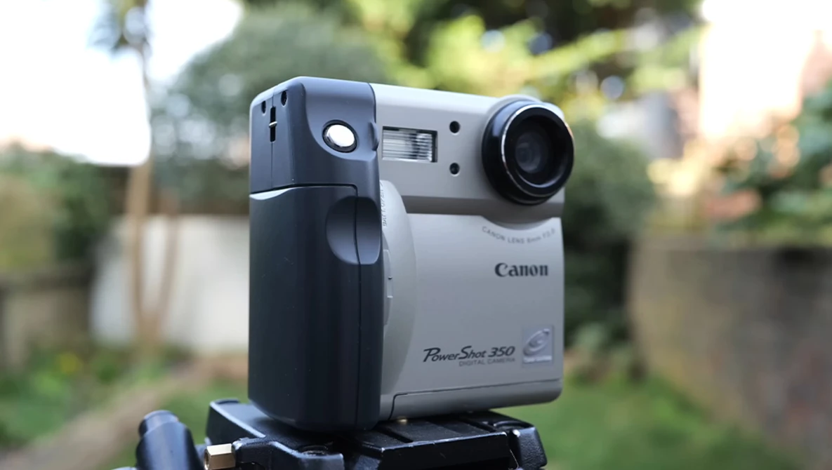 Canon PowerShot 350 digital camera mounted on a tripod, photographed outdoors with blurred garden background.