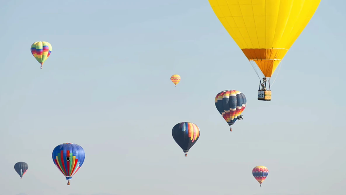 Multiple hot air balloons in flight against a clear blue sky at various altitudes and distances.
