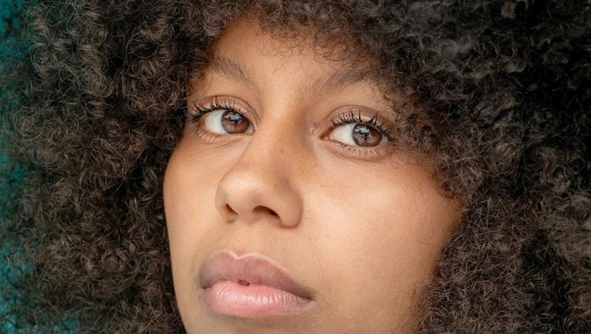Portrait of a woman with curly dark hair looking upward with a contemplative expression.