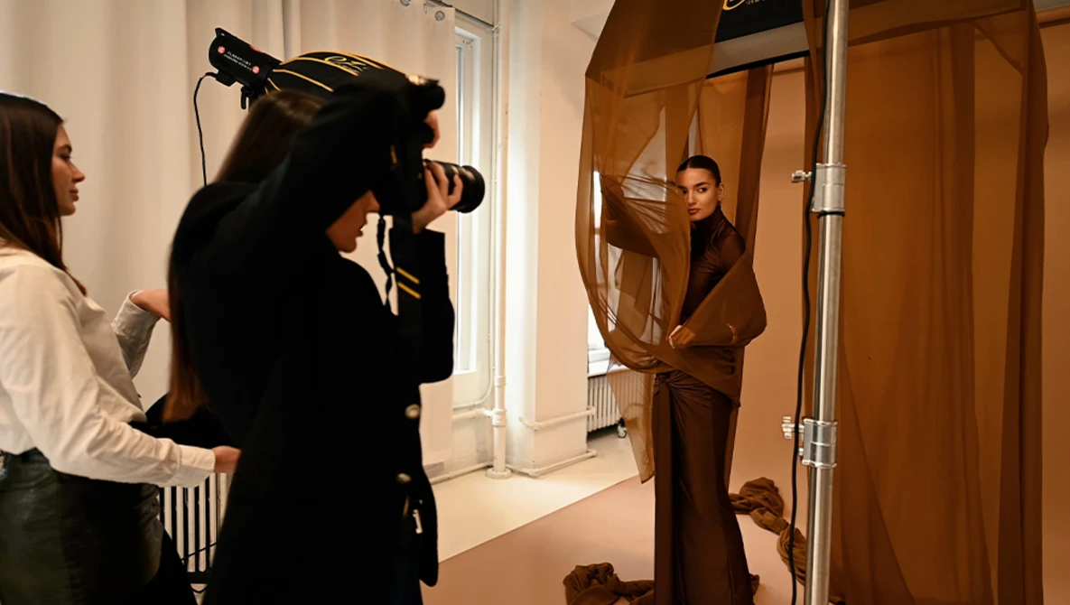 Videographer operating professional camera during an indoor fashion or portrait shoot in a minimalist studio space.