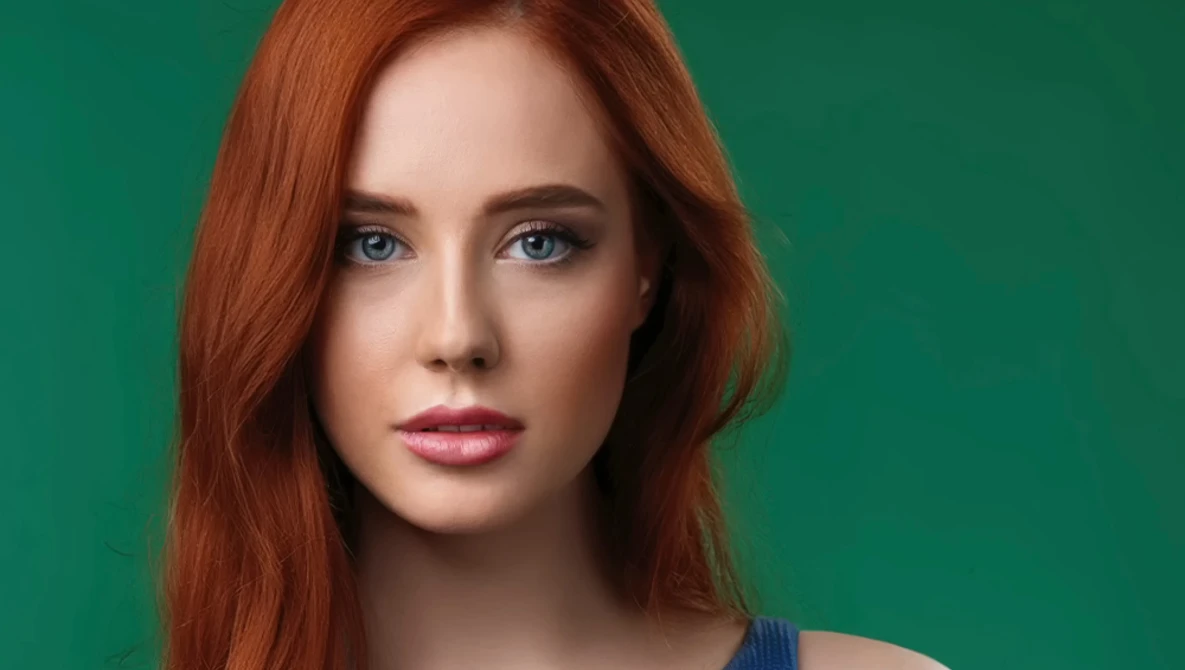 Woman with long reddish-brown hair and blue eyes against a solid green background.
