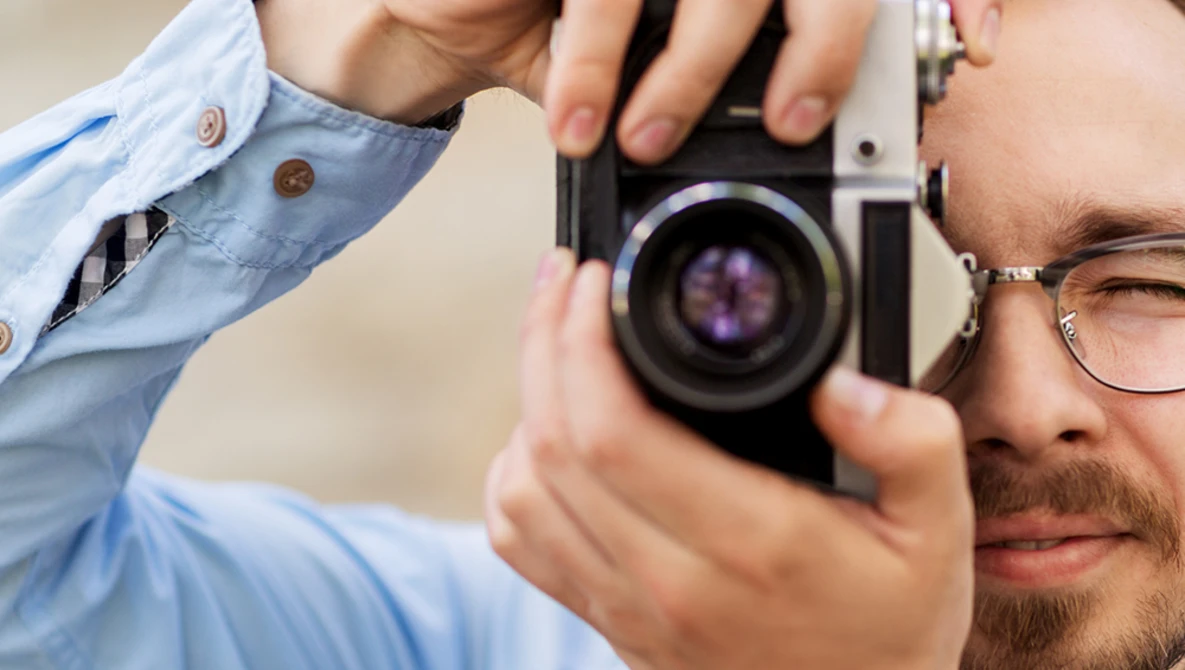 Photographer holding a rangefinder film camera up to his eye to compose a shot.