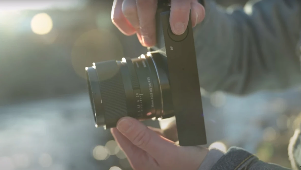 Photographer's hands holding a vintage manual focus lens against a blurred outdoor background in golden sunlight.