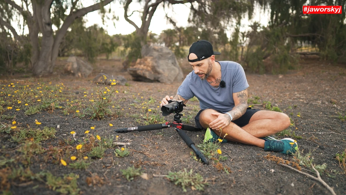 Videographer crouching while operating a camera mounted on a stabilizer rig in an arid outdoor landscape.