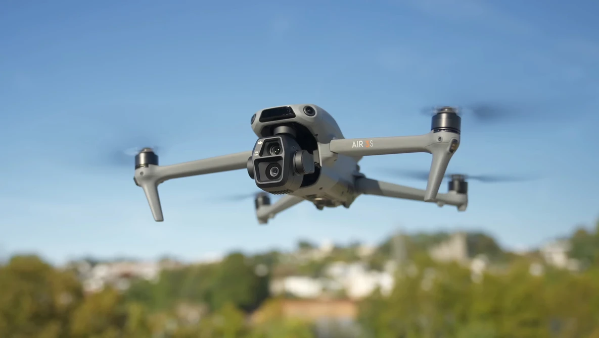 DJI Air 3 drone hovering in flight against blue sky with suburban landscape below.