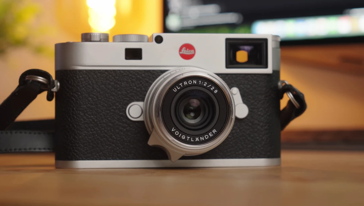 Leica M camera with silver and black body, Ultron lens, sitting on wooden surface with warm lighting.