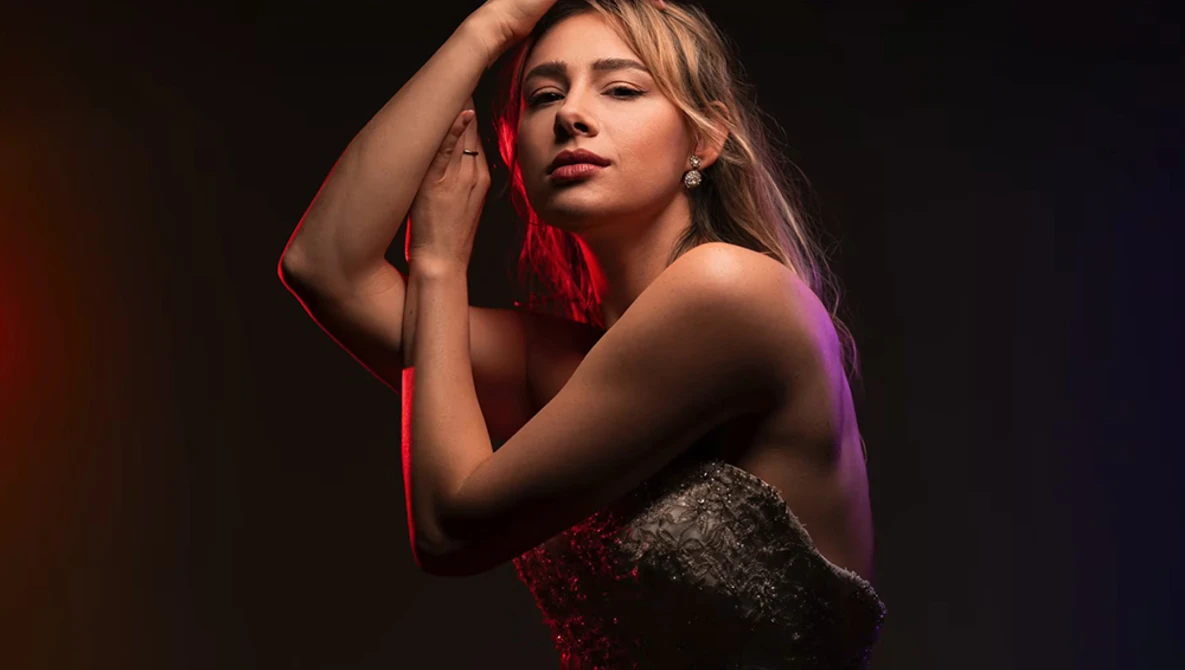Woman posed against dark background with red and purple gel lighting.