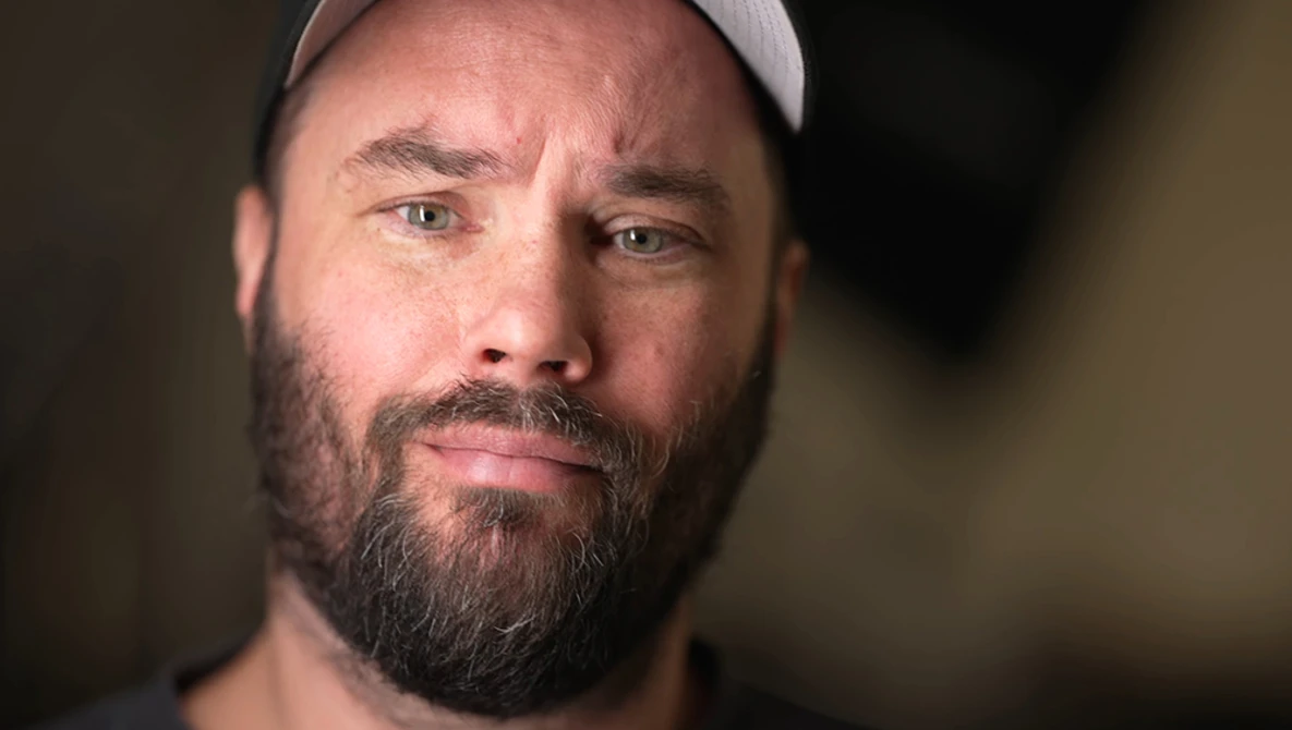 Bearded man wearing a light gray cap, looking directly at camera with a serious expression.