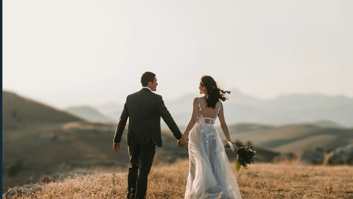 Bride and groom walking hand-in-hand through a golden harvest field at dusk.