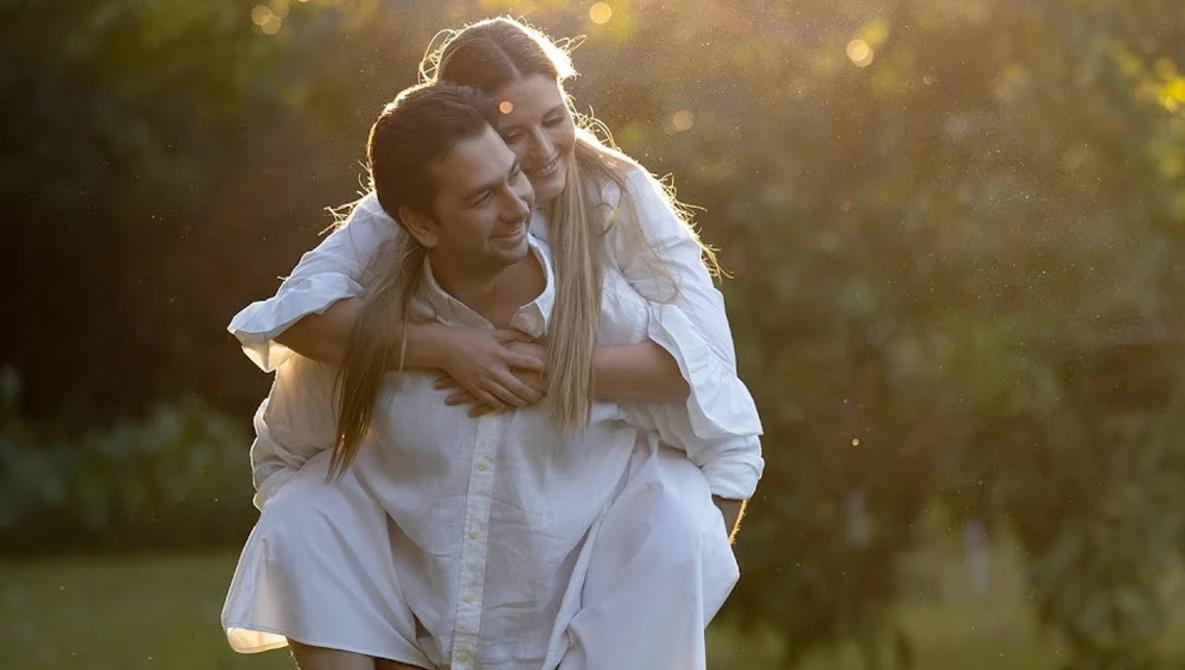 Man in white shirt giving piggyback ride to woman in golden-hour sunlight.