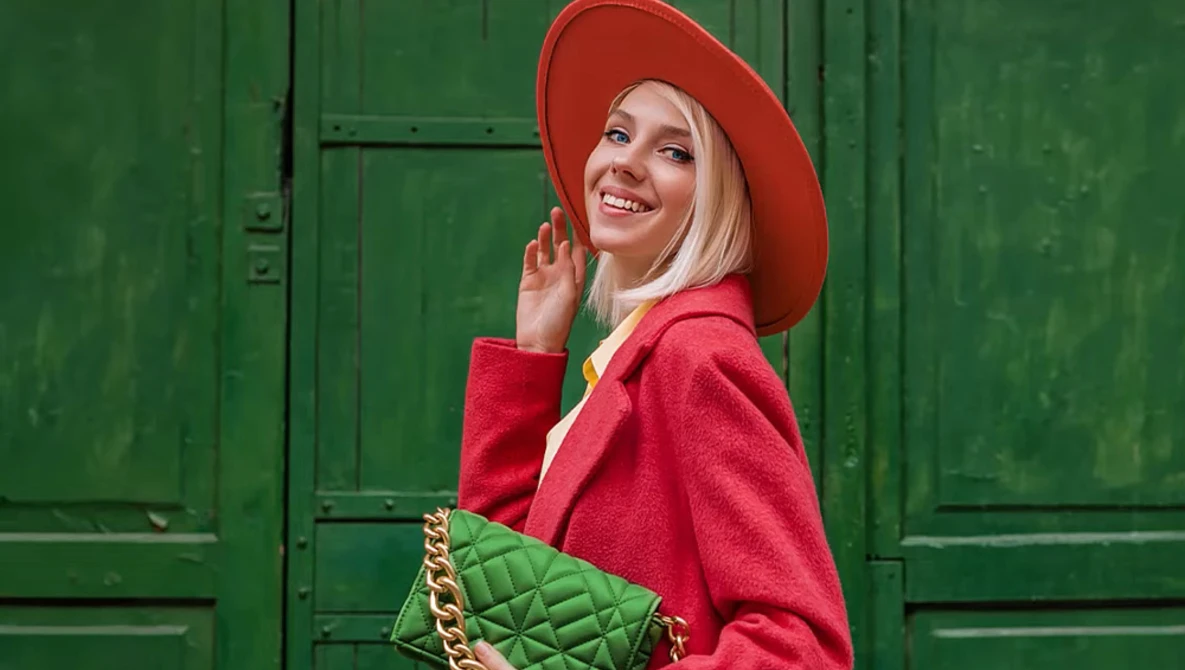 Woman in red coat and hat poses against a green door, holding a quilted green handbag.