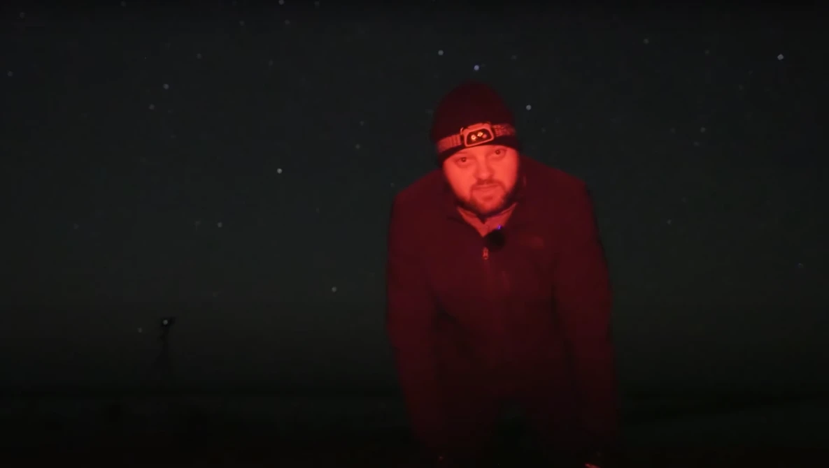 Person wearing deep red jacket and beanie with headlamp in dark night setting with stars.