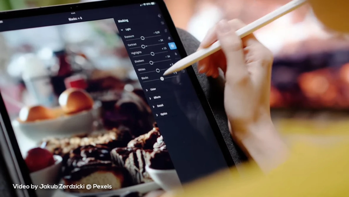 Photographer using stylus on tablet displaying food photography with adjustment panel open.