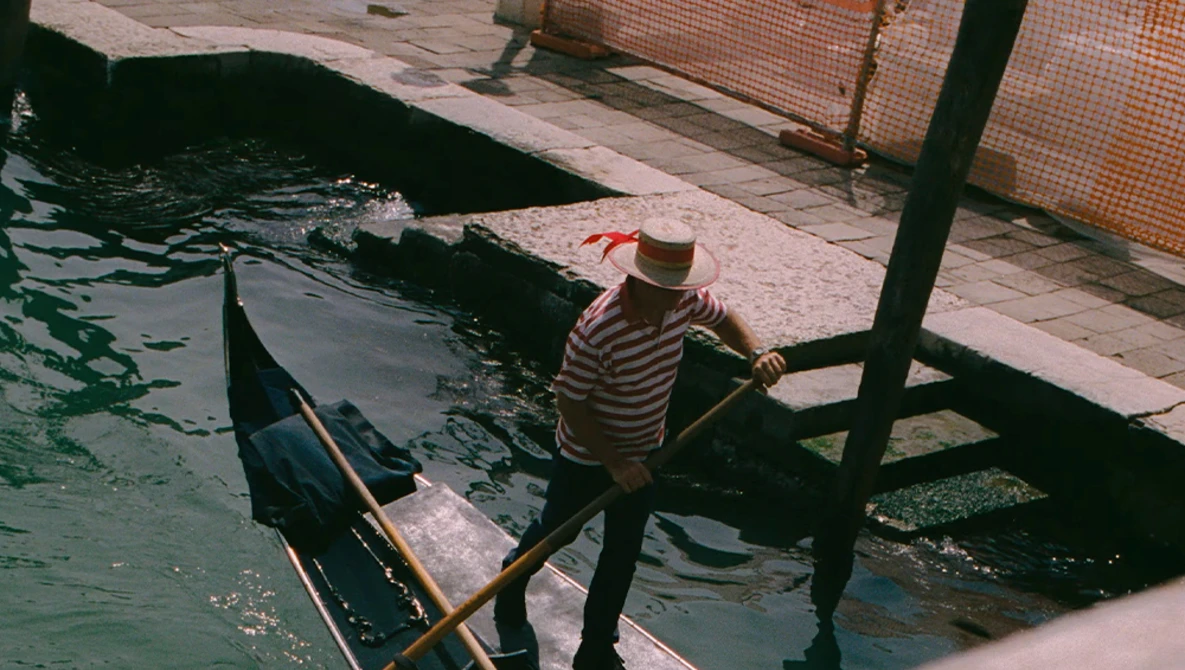 Gondolier in striped shirt standing in gondola at dock, preparing boat or waiting for passengers.