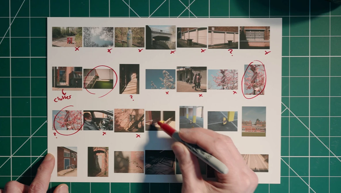 Contact sheet of architectural and landscape photographs laid flat on a cutting mat with hands marking selections in red.