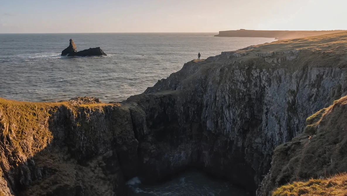 Dramatic coastal cliffs at golden hour with a sea stack and distant headlands across calm waters.