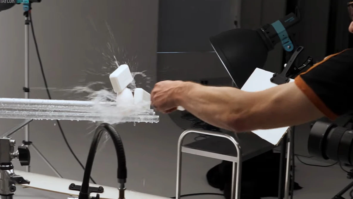 Photographer's hand adjusting a product on a white platform during a studio shoot with key lighting setup.