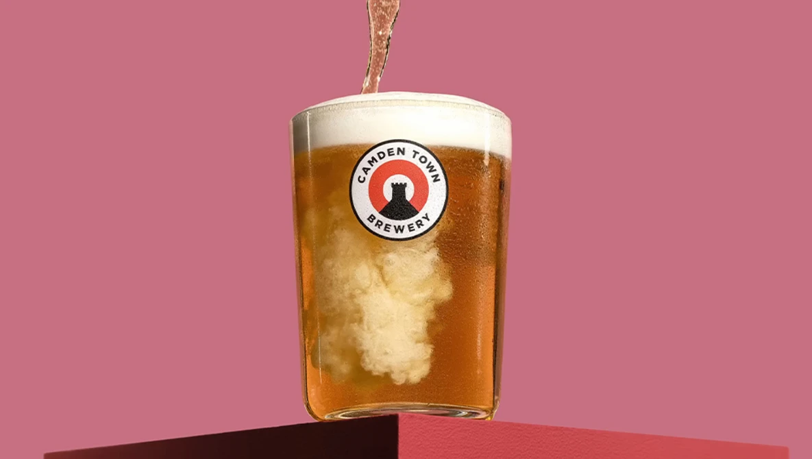 Beer being poured into a glass with brewery logo against a pink background.