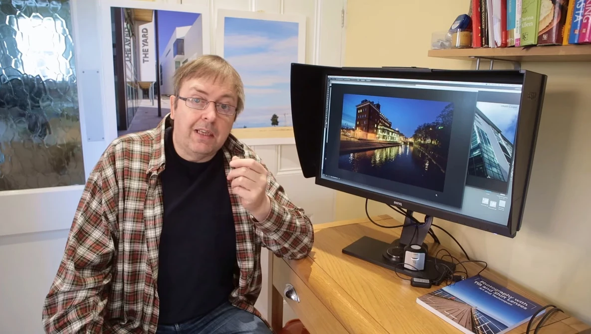 Photographer in plaid shirt at desk reviewing architectural images on dual monitors.