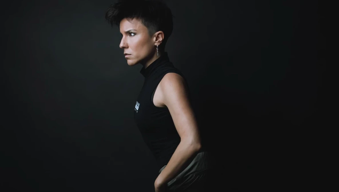 Person in black sleeveless top photographed in profile against dark background.