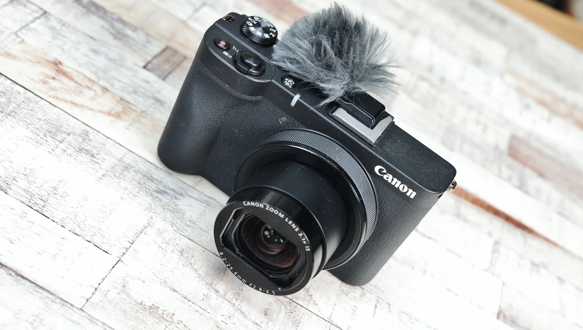 Canon EOS M6 Mark II compact camera with attached microphone on whitewashed wooden surface.