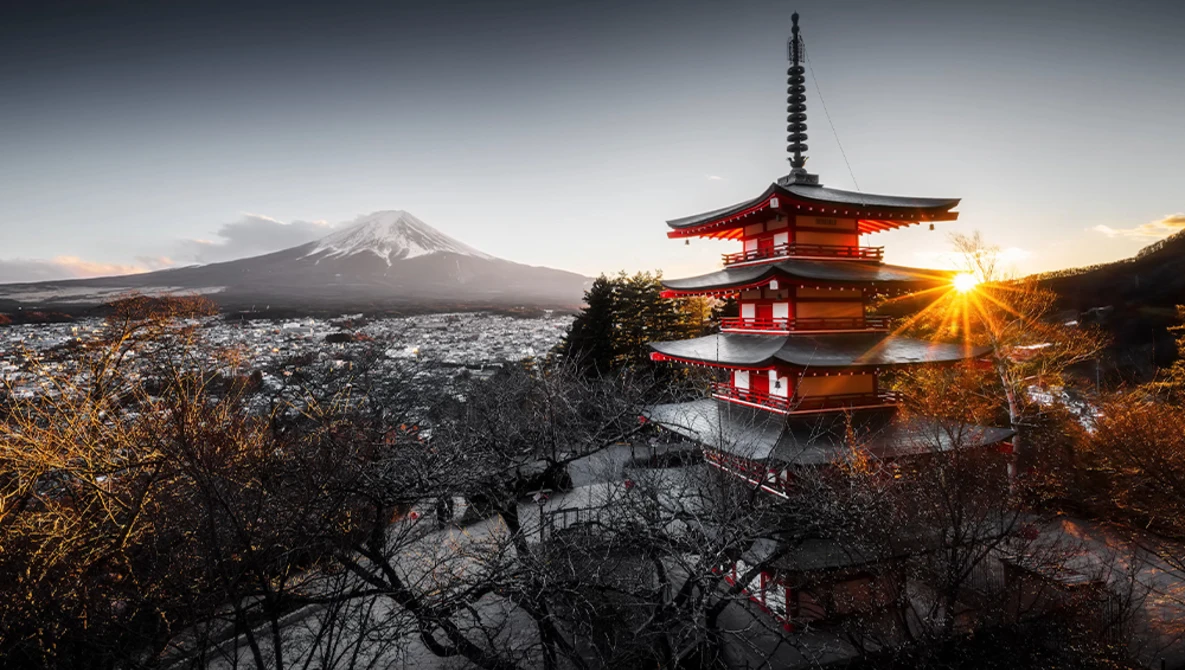 Red pagoda silhouetted against snow-capped mountain at sunset with golden light breaking through.