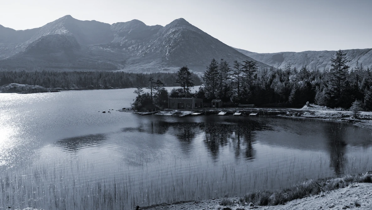 Snow-covered mountains and coniferous forest reflected in a partially frozen alpine lake.