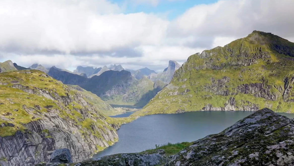 Alpine lake nestled between steep moss-covered mountains under partly cloudy sky.
