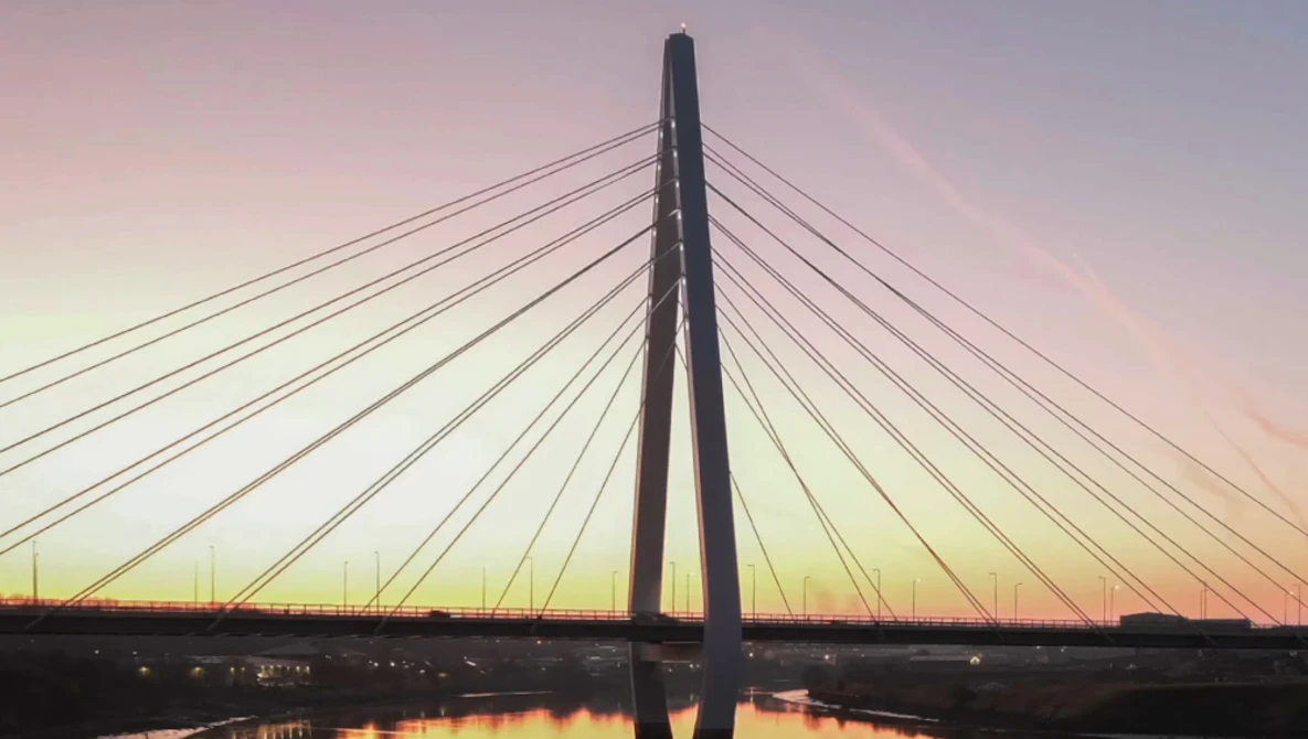 Cable-stayed bridge silhouetted against a dusky sky with golden and pink hues reflected in still water below.