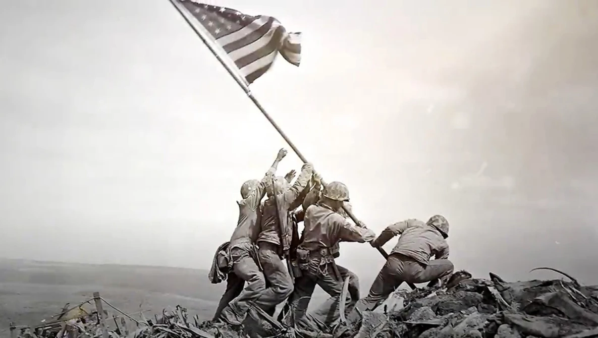 Soldiers raising an American flag on rocky terrain during overcast conditions.