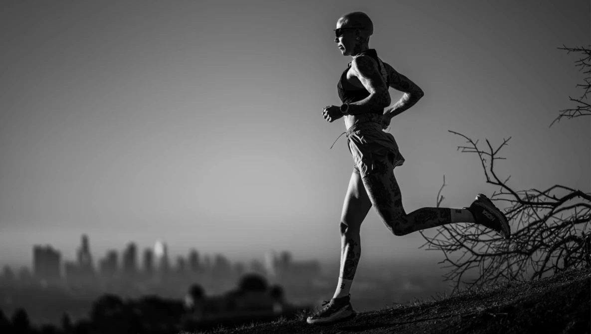 Silhouetted runner jogging on a ridge overlooking a hazy cityscape at dusk.
