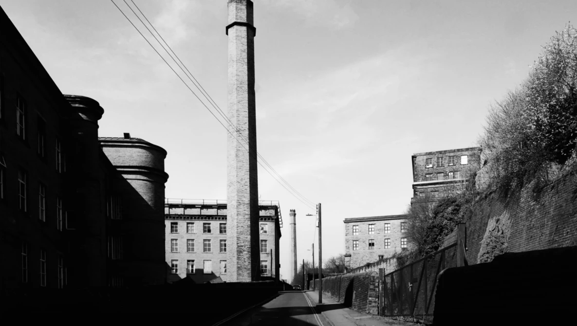 Industrial urban street with tall chimney and apartment buildings in black and white.