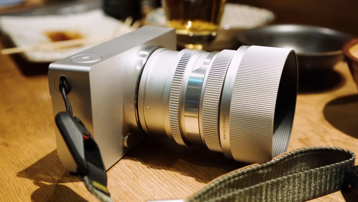 White mirrorless camera with silver telephoto lens on wooden table.