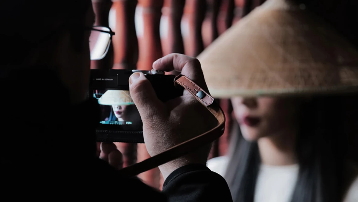Cinematographer holding a professional video camera with monitor attachment in dark indoor venue.