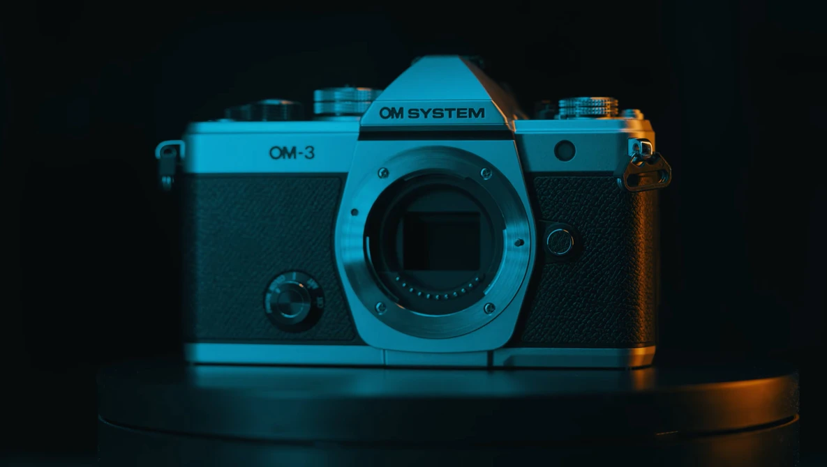 OM System OM-3 rangefinder camera with cyan and orange gel lighting against dark background.