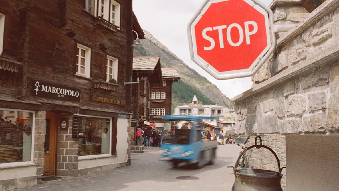 Alpine village street with red stop sign, motion-blurred vehicle, and traditional stone buildings.