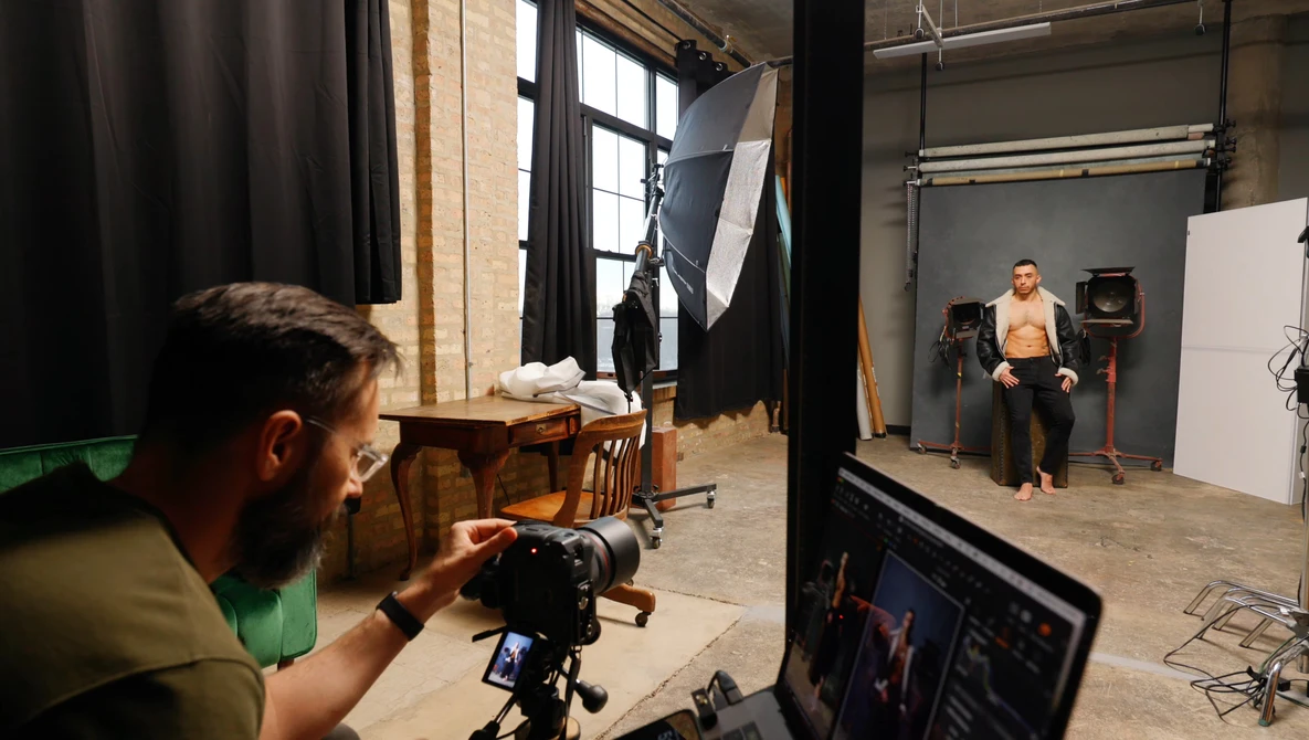 Photographer operating camera on tripod during studio shoot with model and lighting setup.