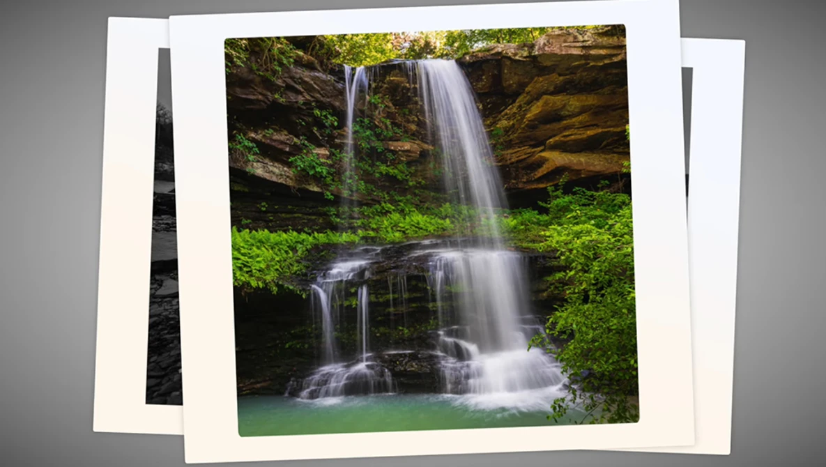 Multi-tiered waterfall cascading into an emerald pool surrounded by moss-covered rocks and lush green vegetation.