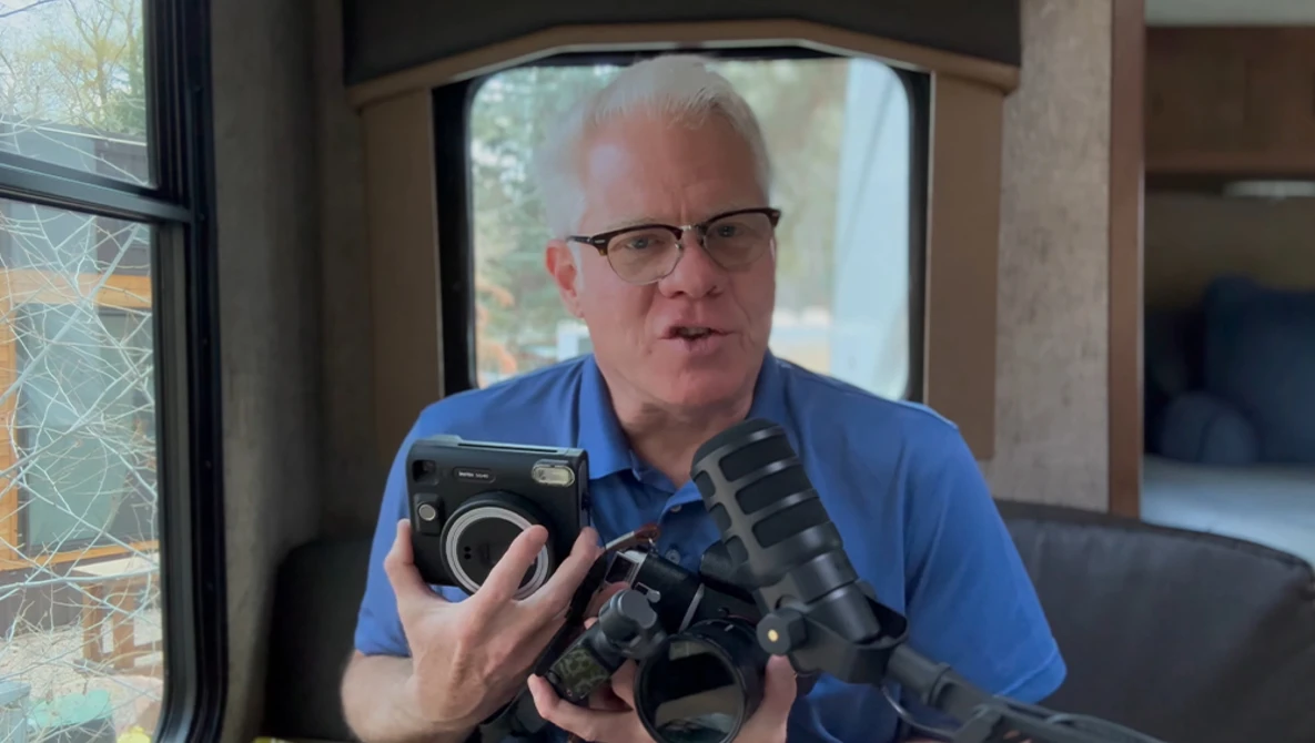 Photographer holding vintage film cameras while wearing glasses and a blue shirt.