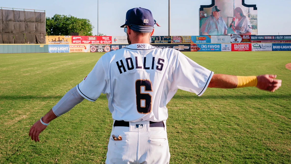 Baseball player wearing number 6 jersey standing on grass field with arms outstretched.