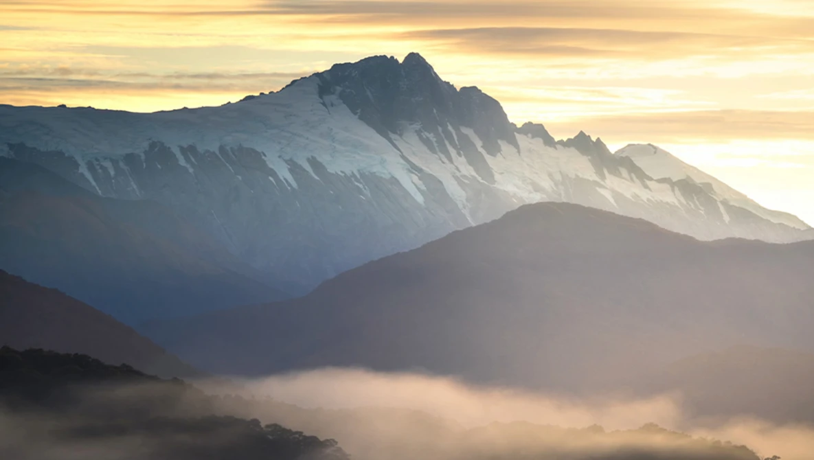Layered mountain peaks bathed in golden sunrise light with misty valleys below.