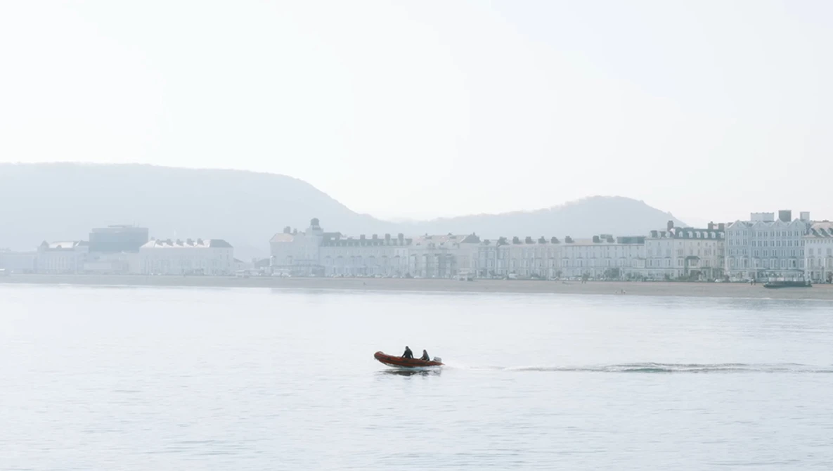 Small red boat on calm water with misty waterfront buildings in the background.