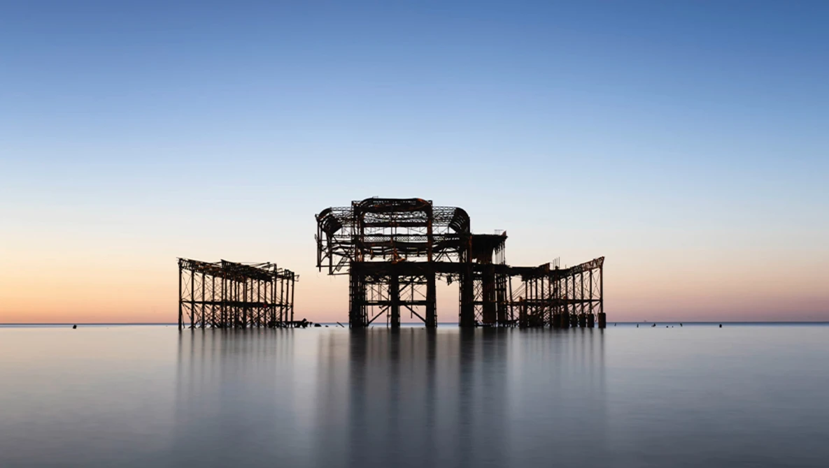 Silhouetted remains of a wooden pier structure at dusk, surrounded by still water.