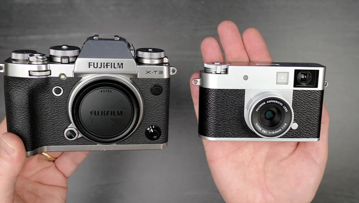 Fujifilm X-T3 mirrorless camera next to a compact rangefinder camera held in hands.